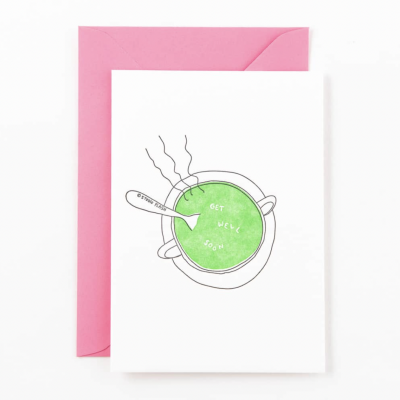 Cartão branco com ilustração de sopa verde e texto GET WELL SOON, com envelope rosa