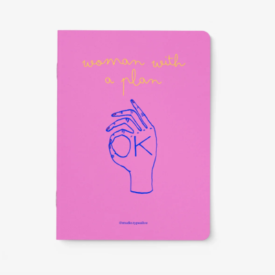 Caderno rosa com desenho de mão azul e texto amarelo woman with a plan.