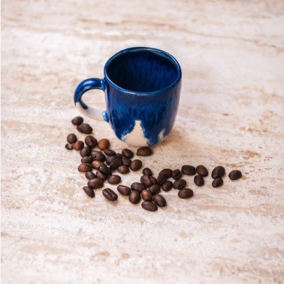 Caneca de cerâmica azul com grãos de café numa superfície clara