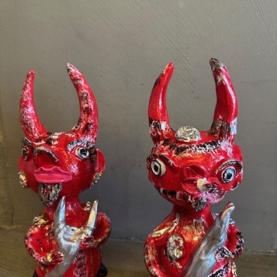 Dois bonecos vermelhos com chifres e olhos grandes segurando objectos prateados