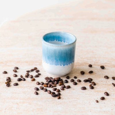 Copo cerâmico azul degradê com grãos de café ao redor