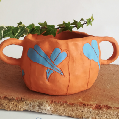 Vaso de cerâmica laranja com folhas azuis e planta verde