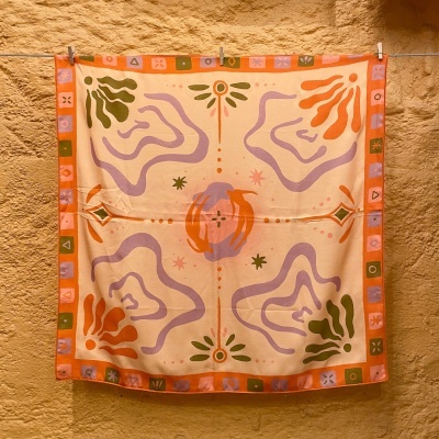 Lenço quadrado com padrão abstrato colorido pendurado numa parede de pedra