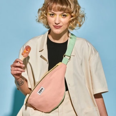 Mala de corpo cor-de-rosa com tira verde usada por mulher em camisola bege, fundo azul