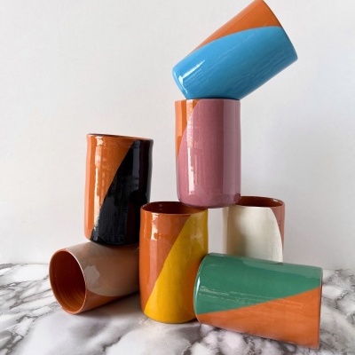 Seis copos de cerâmica coloridos com padrão geométrico sobre uma mesa branca com padrão de mármore cinzento.