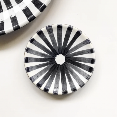 Prato cerâmico redondo com riscas pretas e brancas num padrão radial.