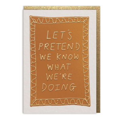 Cartão castanho com texto LETS PRETEND WE KNOW WHAT WERE DOING em relevo dourado