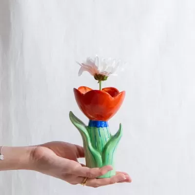 Vaso decorativo de cerâmica com flor branca, mão segurando, fundo branco