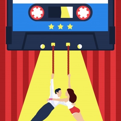 Cassete azul e preto com texto REWRITE THE STARS e duas pessoas penduradas em cordas sob luz amarela