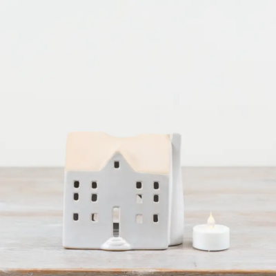 Casa decorativa em cerâmica branca com telhado bege e vela de chá LED ao lado