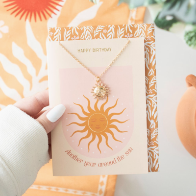 Colar dourado com pendente de sol em cartão decorativo com texto em inglês 