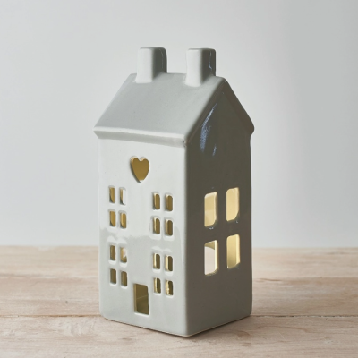 Vela decorativa em forma de casa branca com janelas e coração iluminada