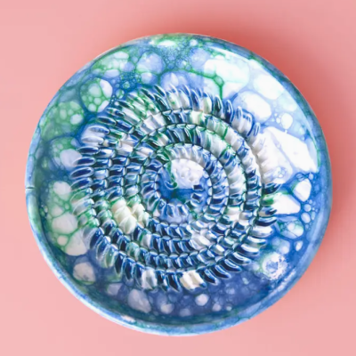 Prato cerâmico colorido com padrão espiral em relevo azul, branco e verde num fundo rosa