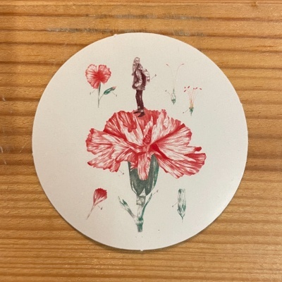 Suporte redondo com ilustração de flor vermelha e figura humana sobre uma superfície de madeira