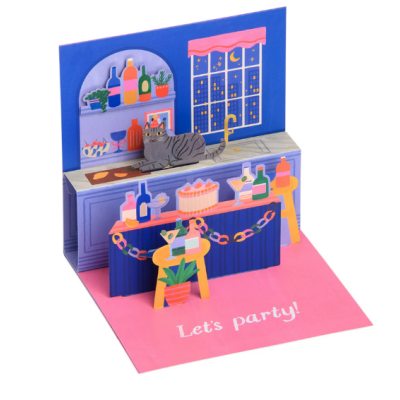 Cartão pop-up de festa num bar com gato, garrafas, bolo e planta sobre a mesa, fundo azul e rosa com janela e texto