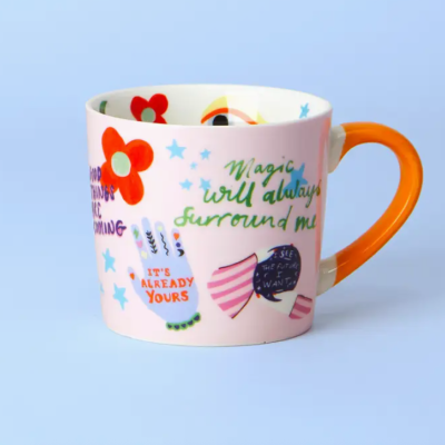 Caneca de cerâmica rosa com alça laranja e várias ilustrações e frases coloridas