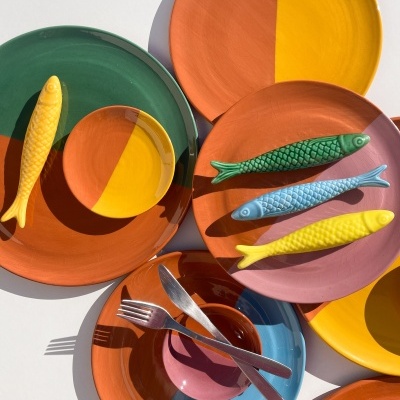 Pratos cerâmicos coloridos com peixes decorativos e talheres sobre superfície branca