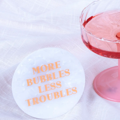 Base para copo branca com texto cor de laranja e copo rosa com bebida rosada