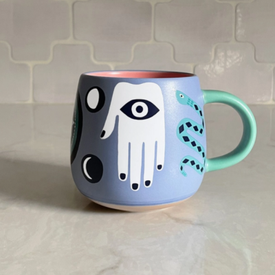 Caneca cerâmica azul claro com desenhos coloridos e pega verde.