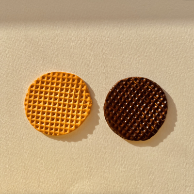 Dois biscoitos redondos com padrão tipo waffle, um amarelo outro de chocolate, sobre fundo claro.