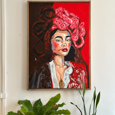 Quadro pintado de mulher com lenço rosa e colar dourado numa parede branca