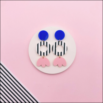 Brincos pendentes com azul, preto e rosa sobre fundo rosa com riscas