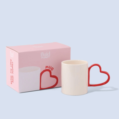 Caneca branca com pega em forma de coração vermelho ao lado da caixa rosa da marca Fluid Market