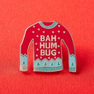 Pin em forma de suéter vermelho com texto BAH HUM BUG e padrões verdes e brancos