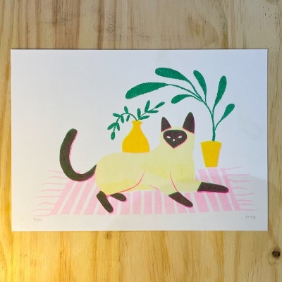 Ilustração de gato branco e preto sobre tapete rosa com plantas em vasos amarelos, impressa em papel branco sobre madeira.
