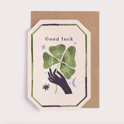 Cartão de boa sorte com ilustração de mão a segurar trevo de quatro folhas e texto Good luck.