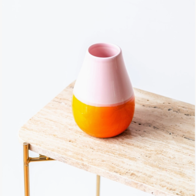 Vaso cerâmico rosa e laranja numa mesa de pedra clara com pés dourados
