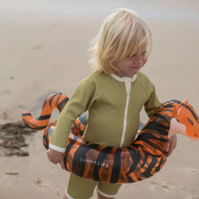 Criança na praia com fato de banho verde e boia insuflável em forma de tigre laranja
