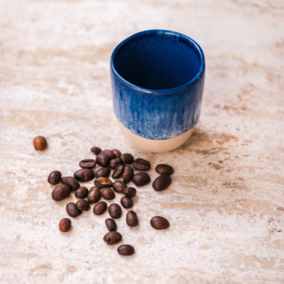 Copo cerâmico azul com feijão de café sobre superfície clara