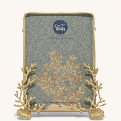 Porta-fotos metálico dourado com suporte coral e concha, ilustração floral e texto decorativo.