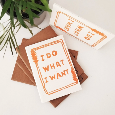 Cartões brancos com texto laranja e envelopes castanhos junto a uma planta verde