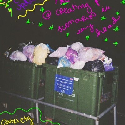 Dois contentores de lixo verdes cheios com sacos de lixo coloridos em ambiente noturno