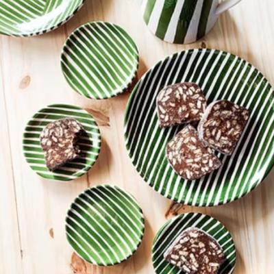 Conjunto de loiça verde e branco com riscas e doce tipo salame de chocolate em mesa de madeira.