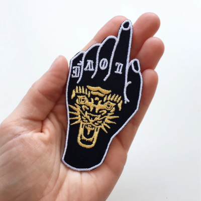 Patch bordado preto em forma de mão com palavras e desenho de felino