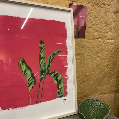 Quadro com pintura de folhas verdes sobre fundo vermelho, prato em forma de folha verde e parede texturada castanha