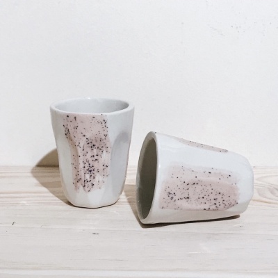 Duas chávenas de cerâmica branca com manchas castanhas e pretas, sobre madeira clara