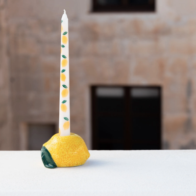 Vela decorativa com suporte em forma de limão sobre superfície branca.