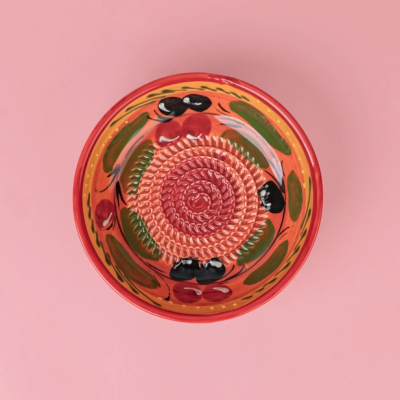 Prato raso em cerâmica pintado com padrão de azeitonas e cerejas sobre fundo rosa.