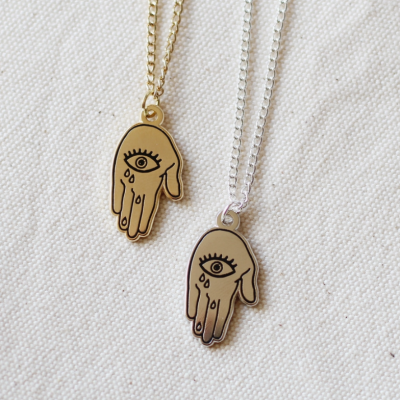 Dois colares com pendentes de mão dourado e prateado com desenho de olho e lágrimas