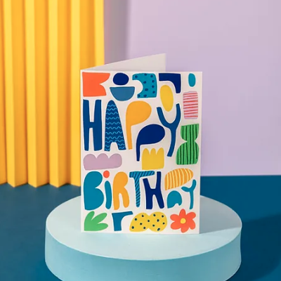Cartão de aniversário colorido sobre base azul com fundo lilás e estrutura amarela