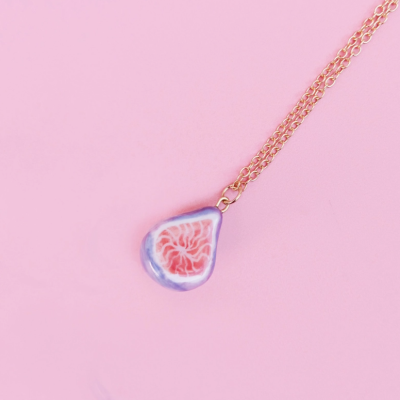 Colar dourado com pendente em forma de gota cor-de-rosa e lilás sobre fundo rosa