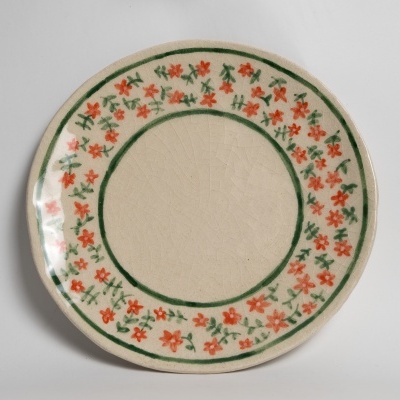Prato redondo de cerâmica decorado com flores vermelhas e folhagem verde