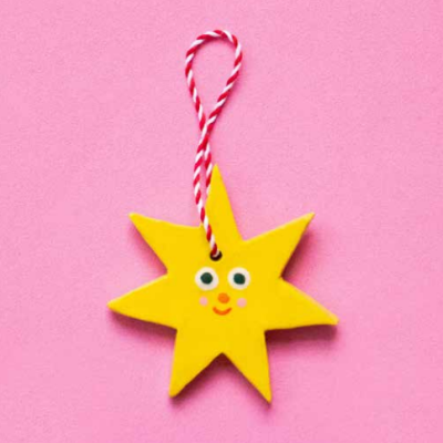 Estrela decorativa amarela com fio vermelho e branco sobre fundo rosa