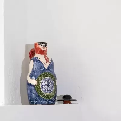 Jarra decorativa em cerâmica com figura feminina em prateleira branca