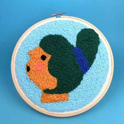 Painel de bordado colorido com rosto estilizado em bastidor redondo