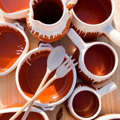 Conjunto de loiça de barro castanho com interior brilhante e utensílios de cozinha de madeira.